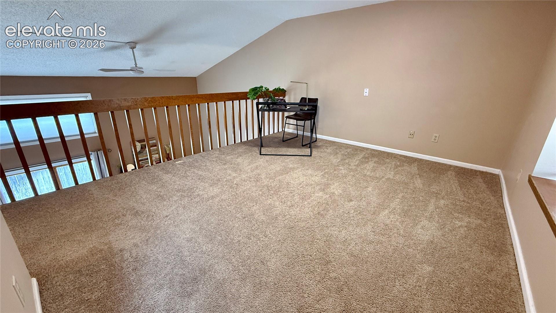 Open loft area featuring vaulted ceilings, wall-to-wall carpeting, and a wooden railing.