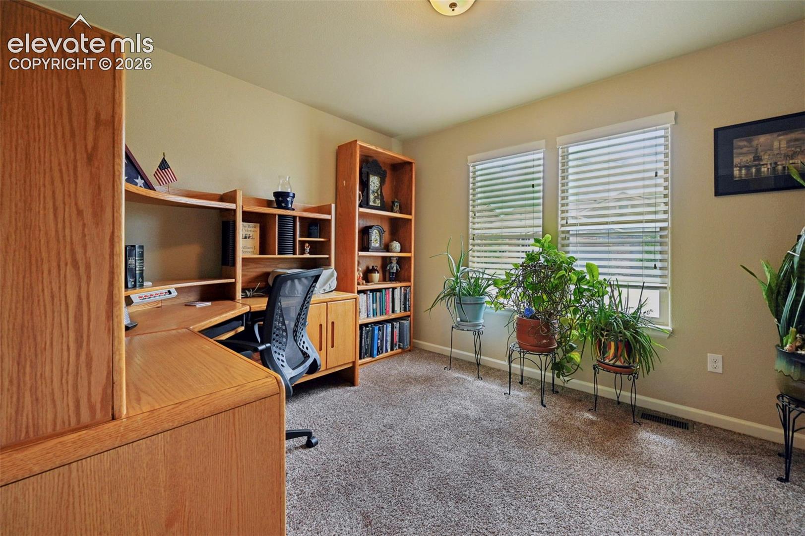 Office featuring two windows with horizontal blinds, neutral wall paint, and textured carpeting