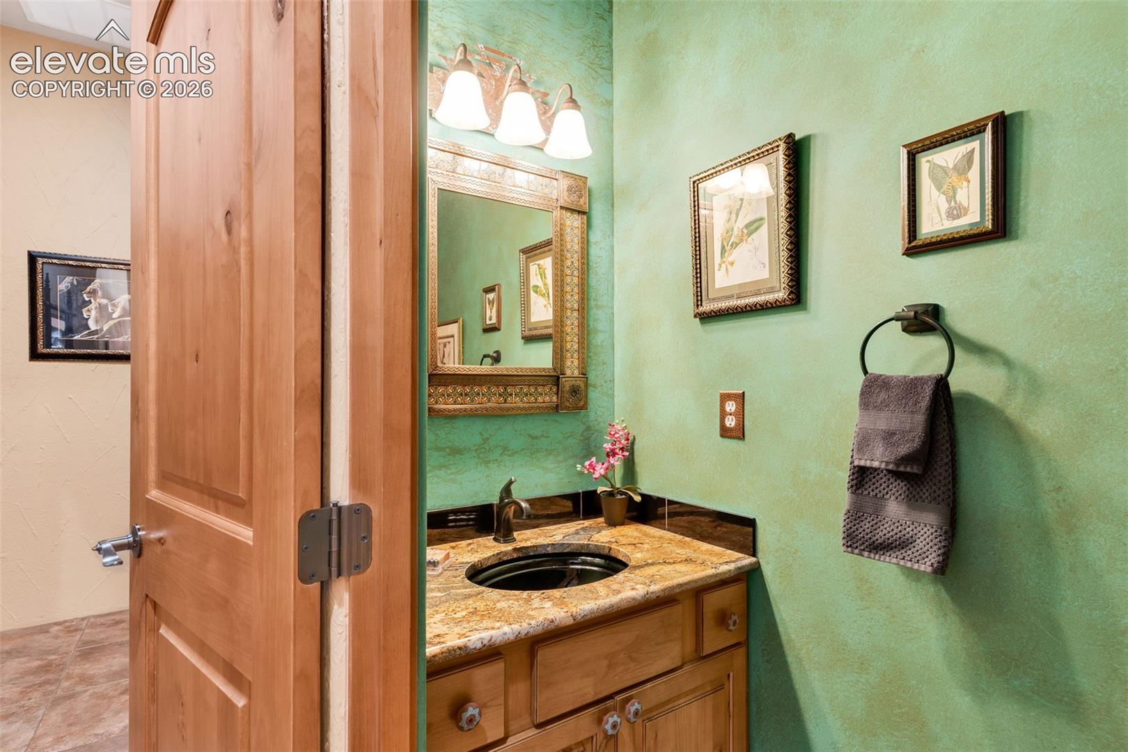 Natural wood door with an arched top, textured green wall finish, stone-surfaced countertop, integrated oval sink, and framed wall-mounted mirror with integrated lighting
