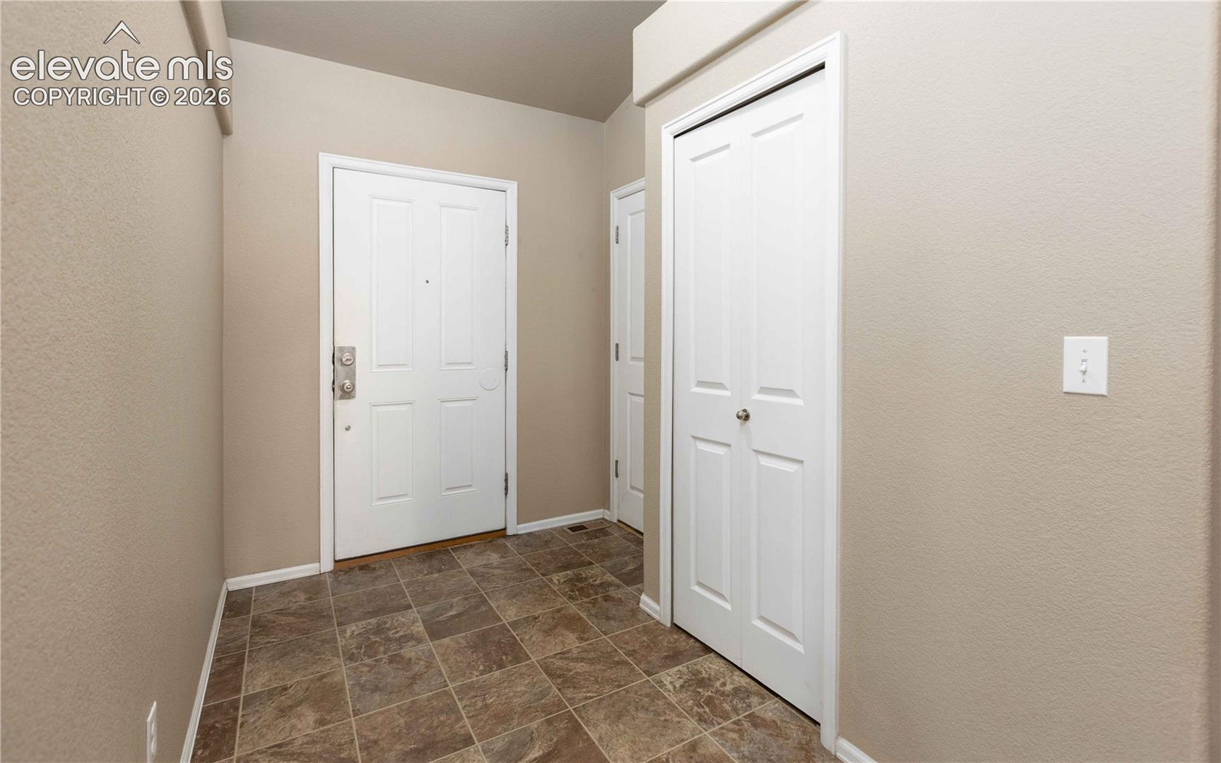 Entryway featuring neutral-toned walls, tile flooring, white paneled doors, and dual-closet storage