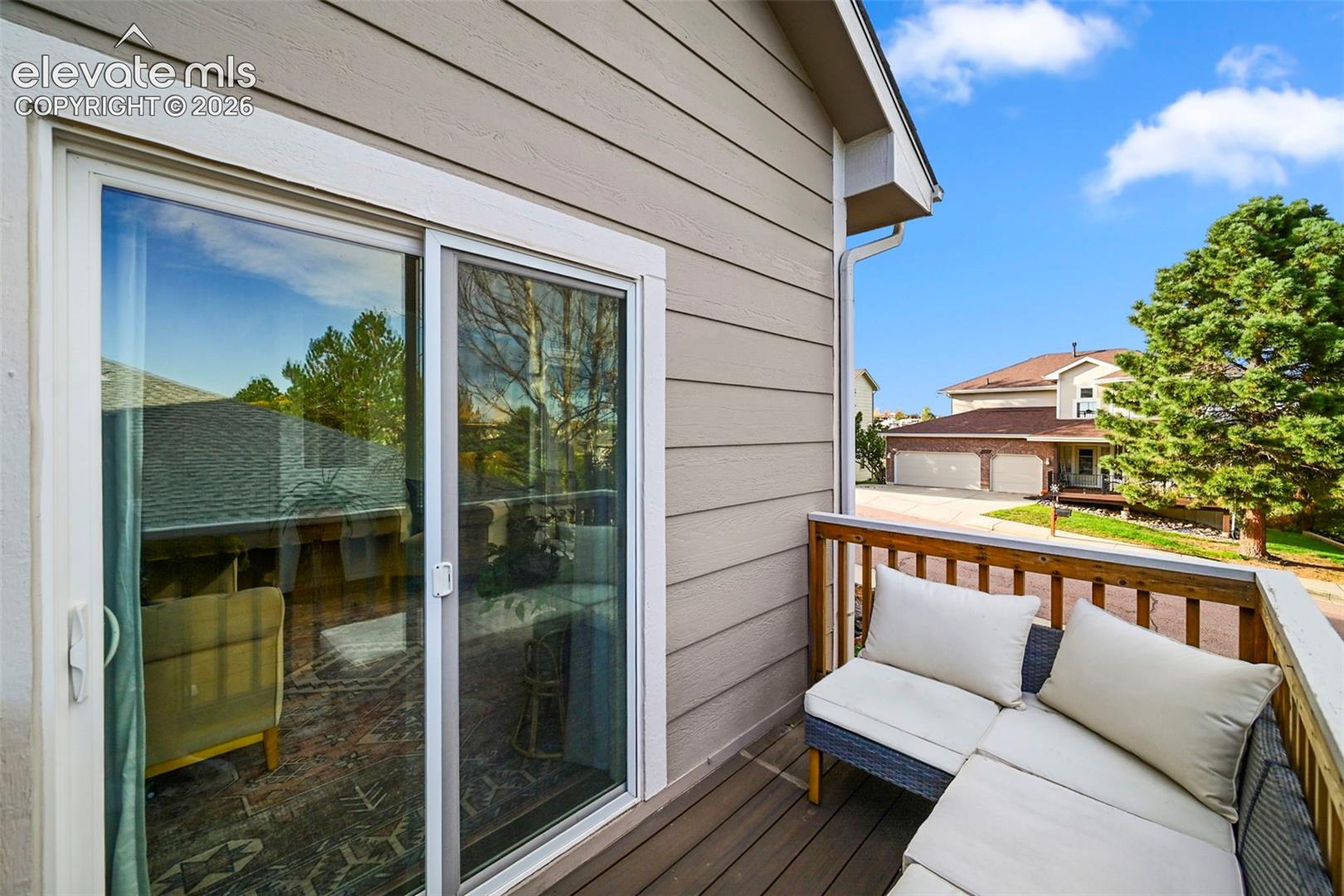 Sliding glass door access to an outdoor balcony, featuring a wood-finish floor and wood slat railing