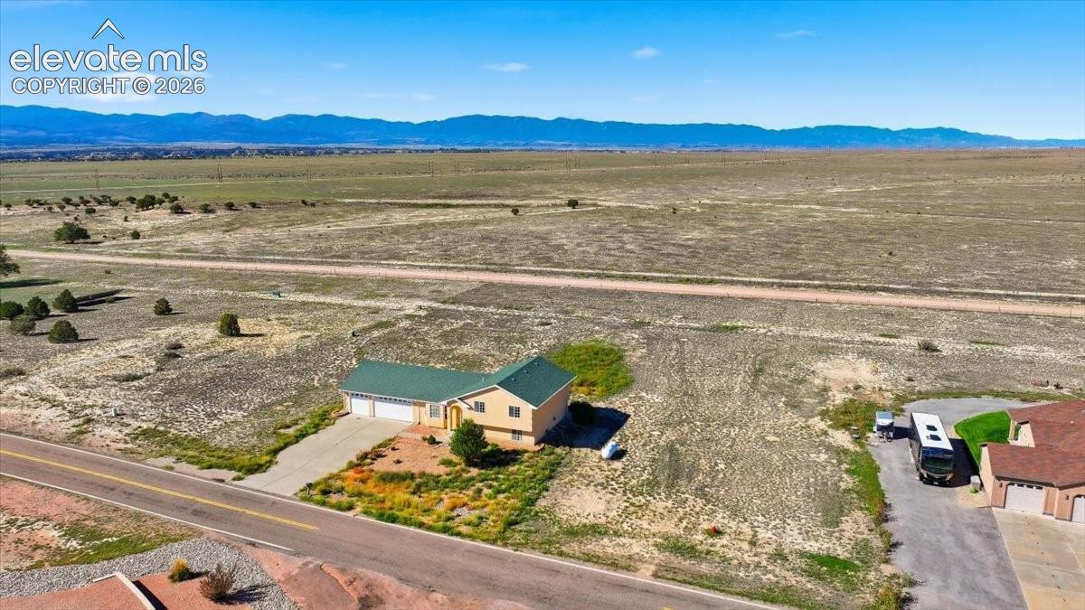 Single-story residence with a green roof, attached two-car garage, and concrete driveway, situated on a large lot with a distant mountain range backdrop