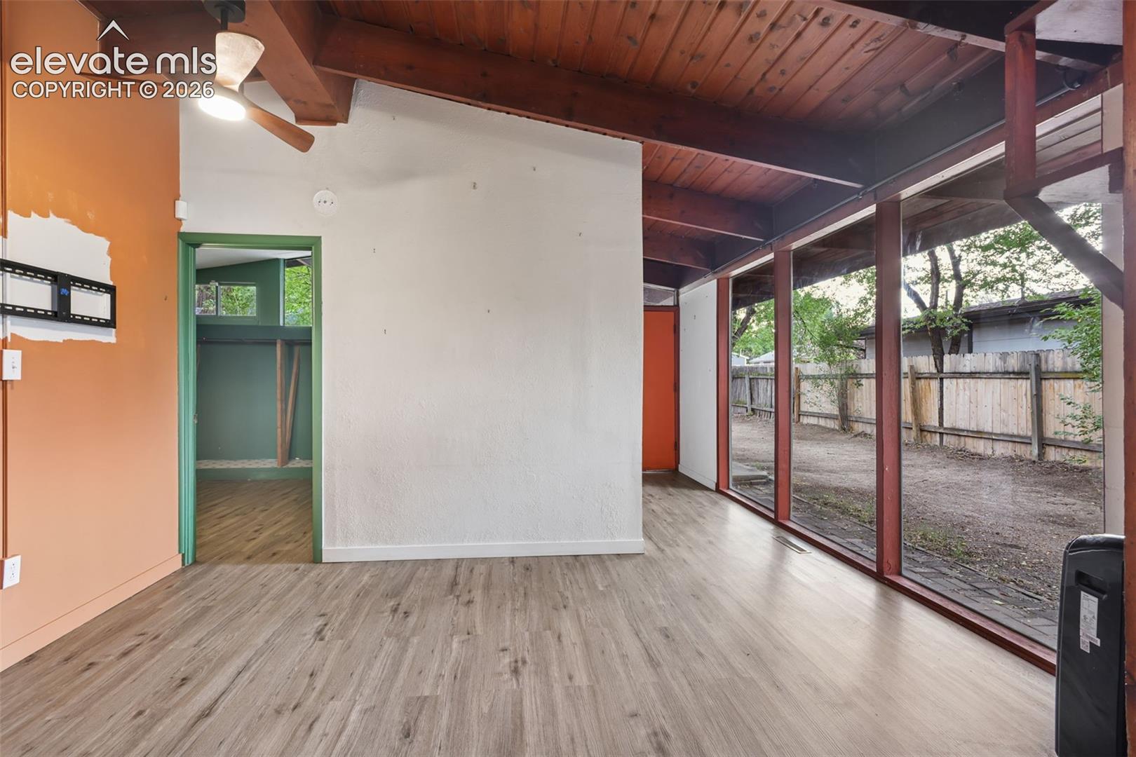 Wood-finish flooring, exposed wood beam ceiling, full-height window panels, wood fence, and ceiling fan