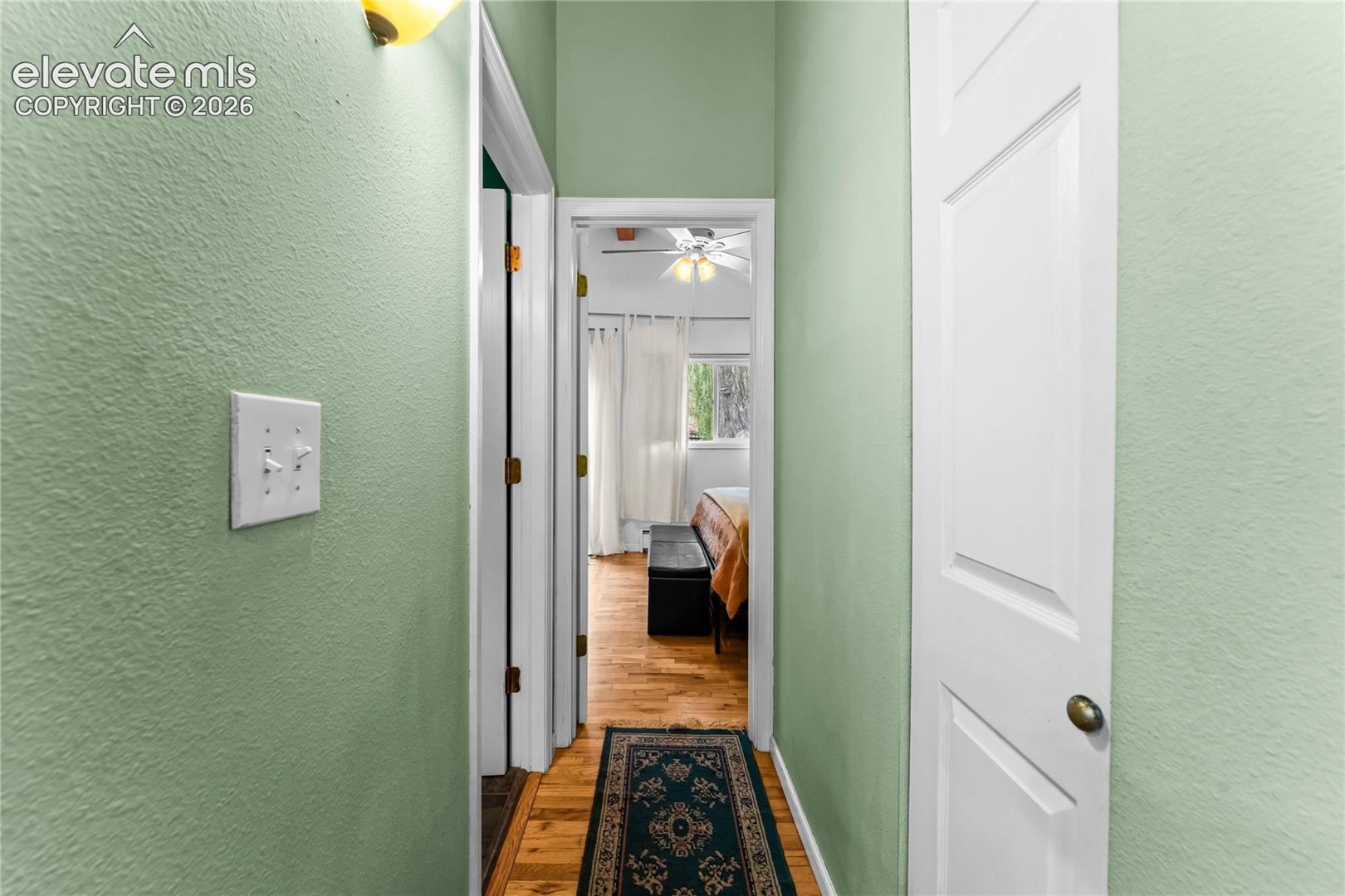 Hallway featuring wood-finish flooring, white paneled interior doors, and overhead wall-mounted lighting