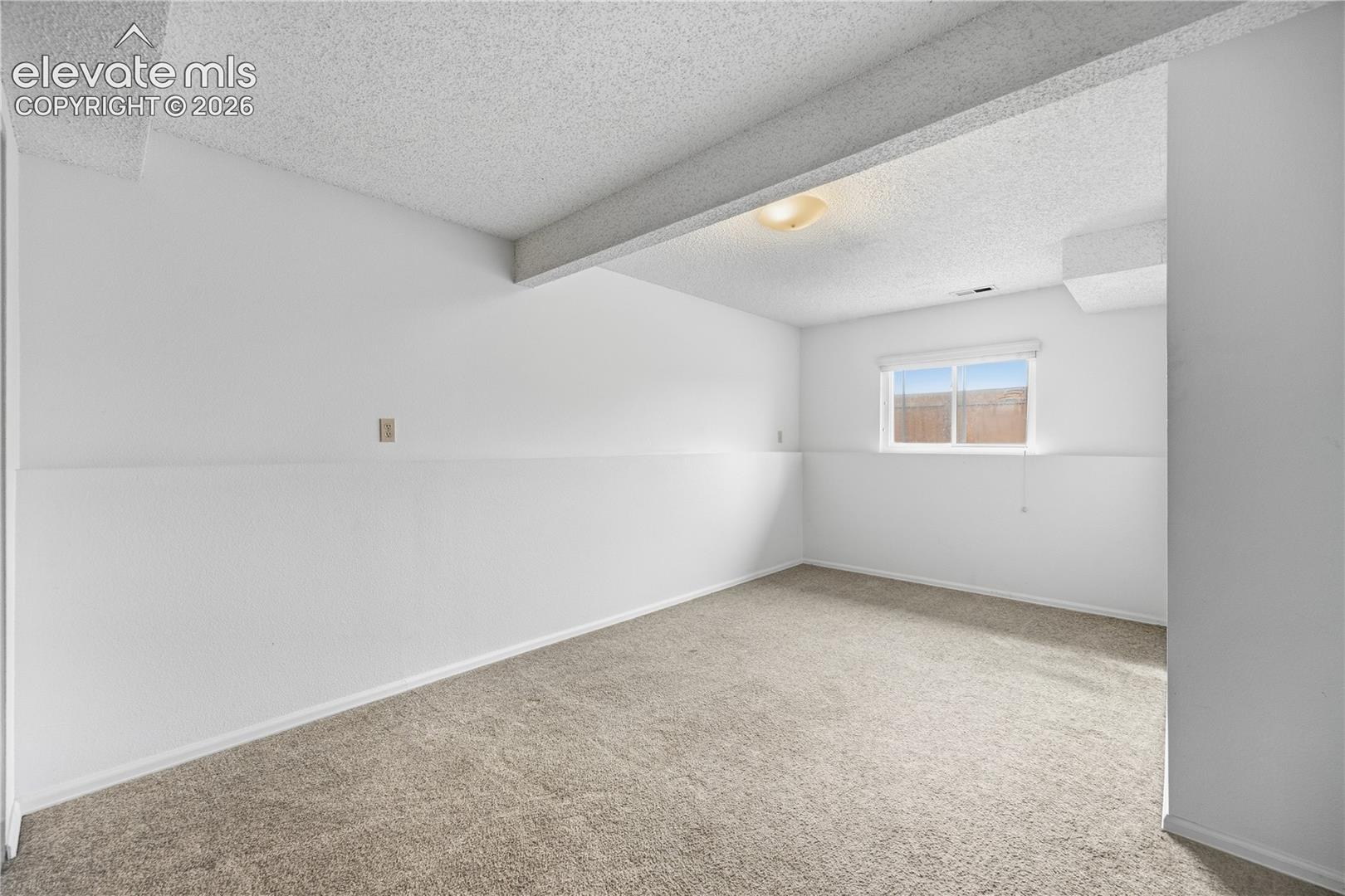 Neutral-toned carpeting, structural ceiling beam, flush-mount lighting, and dual-pane window