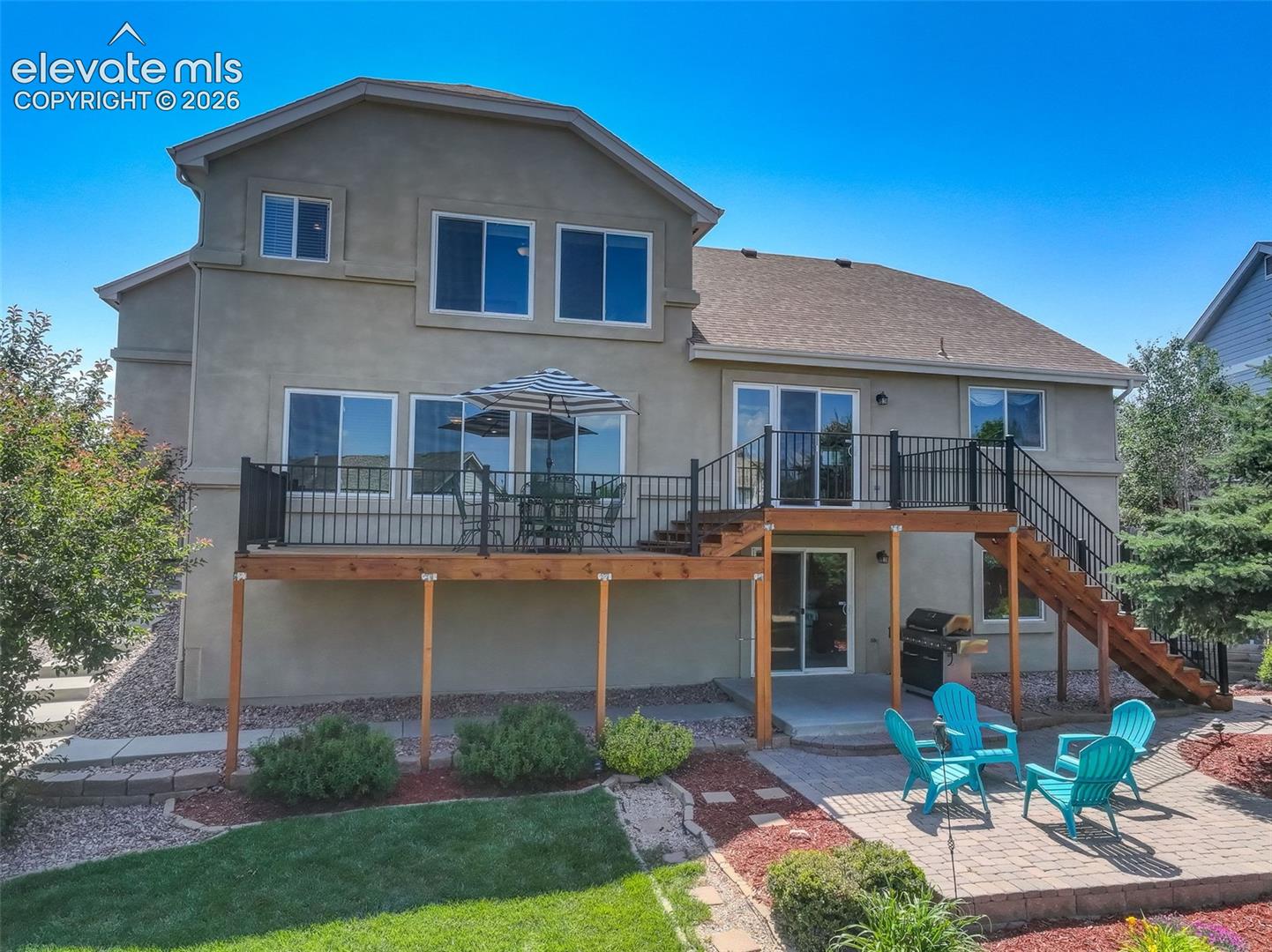 Rear exterior with a multi-level deck featuring black metal railings and a staircase to a paver patio