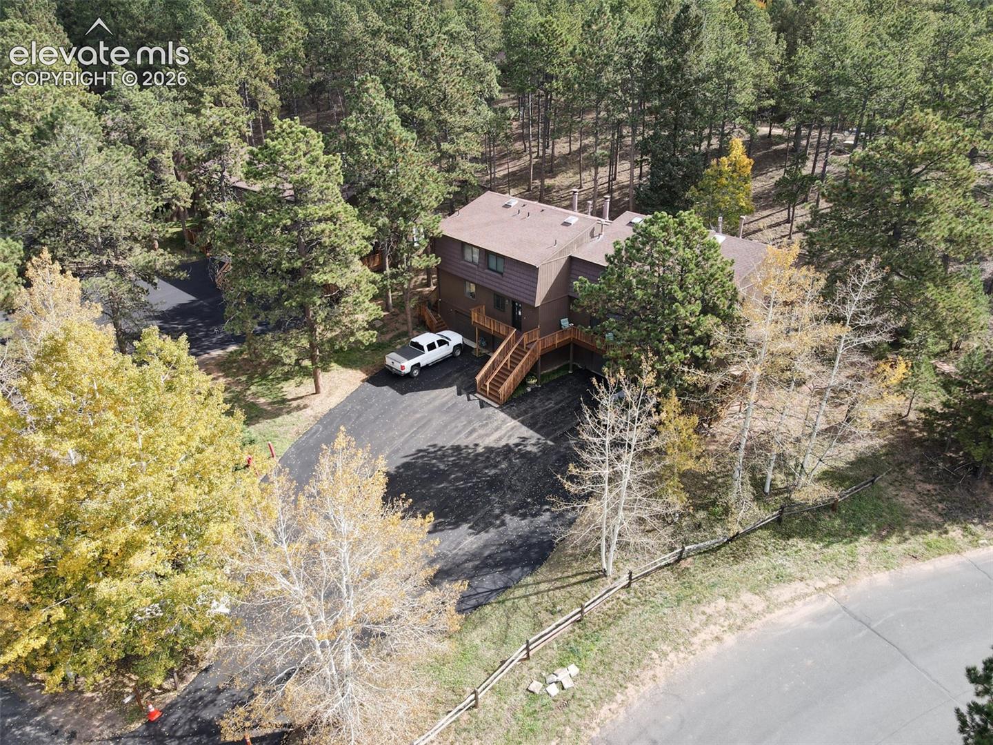 Wood-sided exterior with multiple levels, expansive paved driveway, and natural wood deck