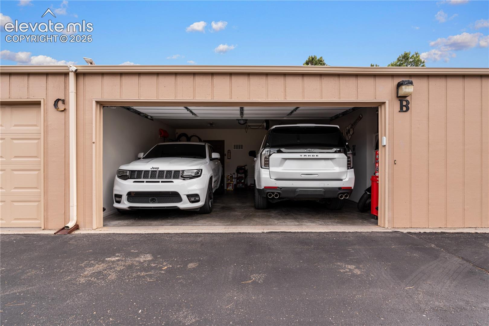Two-car garage with vertical metal siding, concrete flooring, overhead lighting, and an expansive open entry