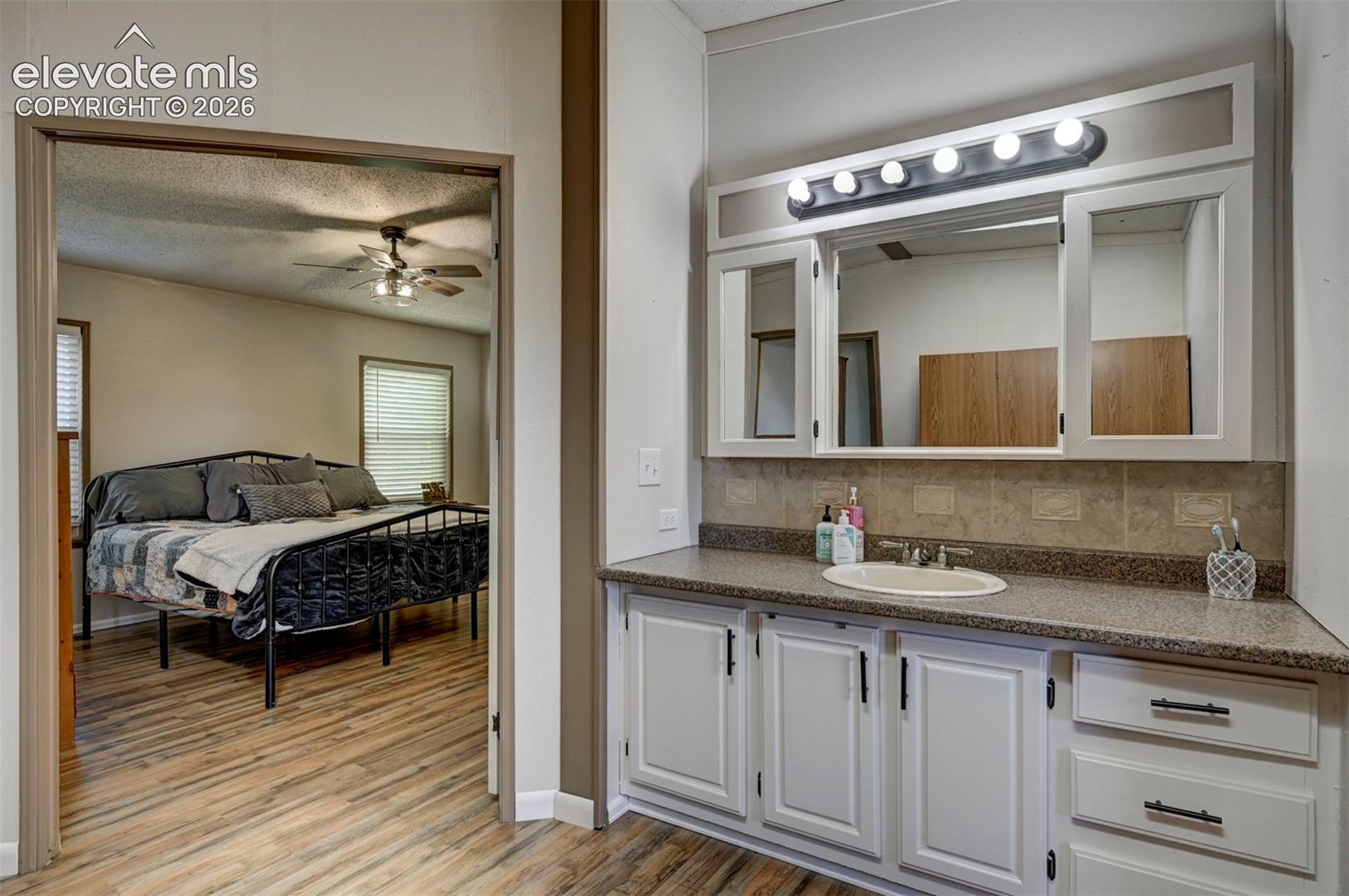 Ensuite bathroom with a textured ceiling, vanity, backsplash, light wood-style flooring, and a ceiling fan