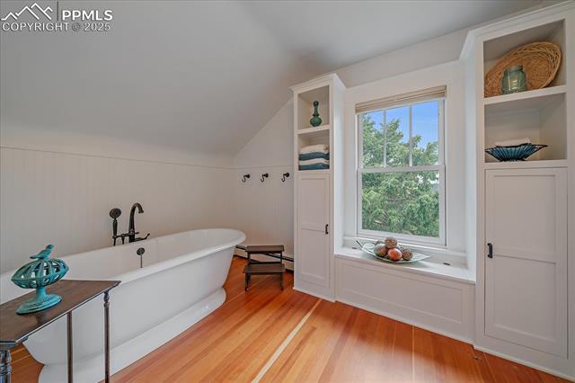 Bathroom featuring a freestanding tub, wood finished floors, lofted ceiling, wainscoting, and a baseboard radiator