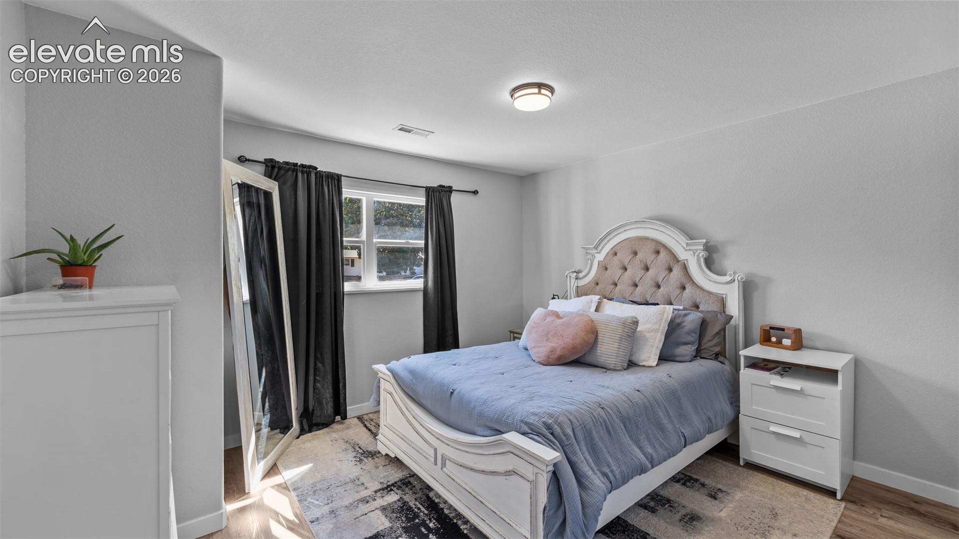 Neutral wall tones, wood-finish flooring, and a single-pane window with a curtain rod assembly