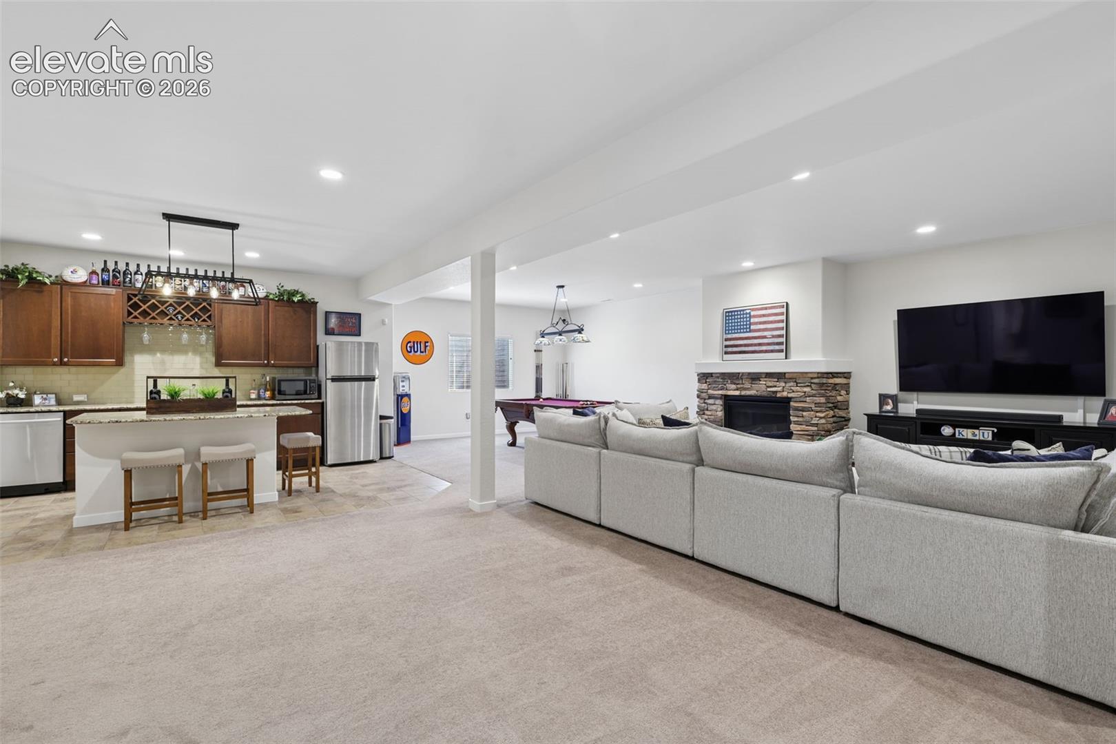 Open-concept finished lower level featuring a full-height stone fireplace, recessed lighting, and a full wet bar with wood cabinetry and a wine rack