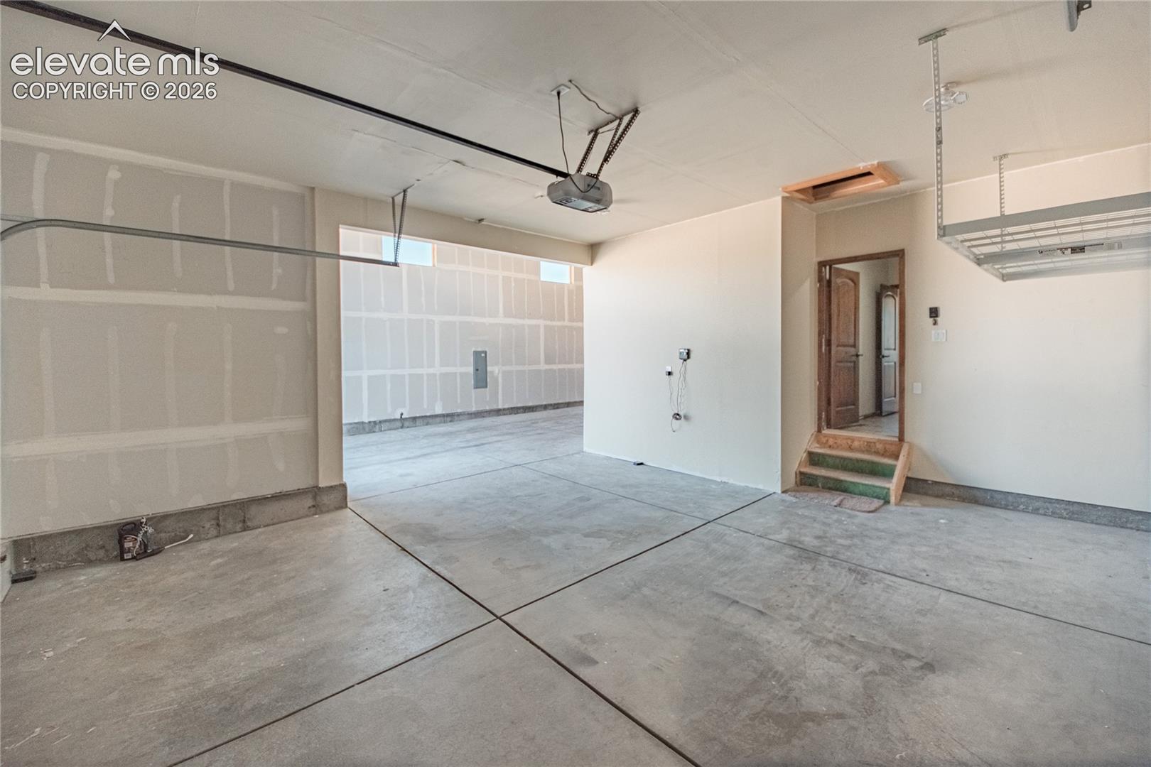 Spacious multi-car garage featuring a concrete floor, an interior access door with wooden steps, and an overhead storage rack