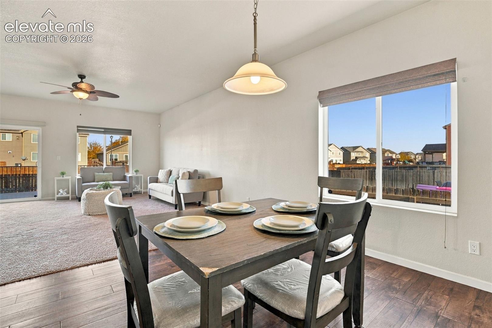 Open-concept floor plan featuring wood-finish flooring, a neutral color palette, a brushed-metal pendant light fixture, and large windows providing natural light