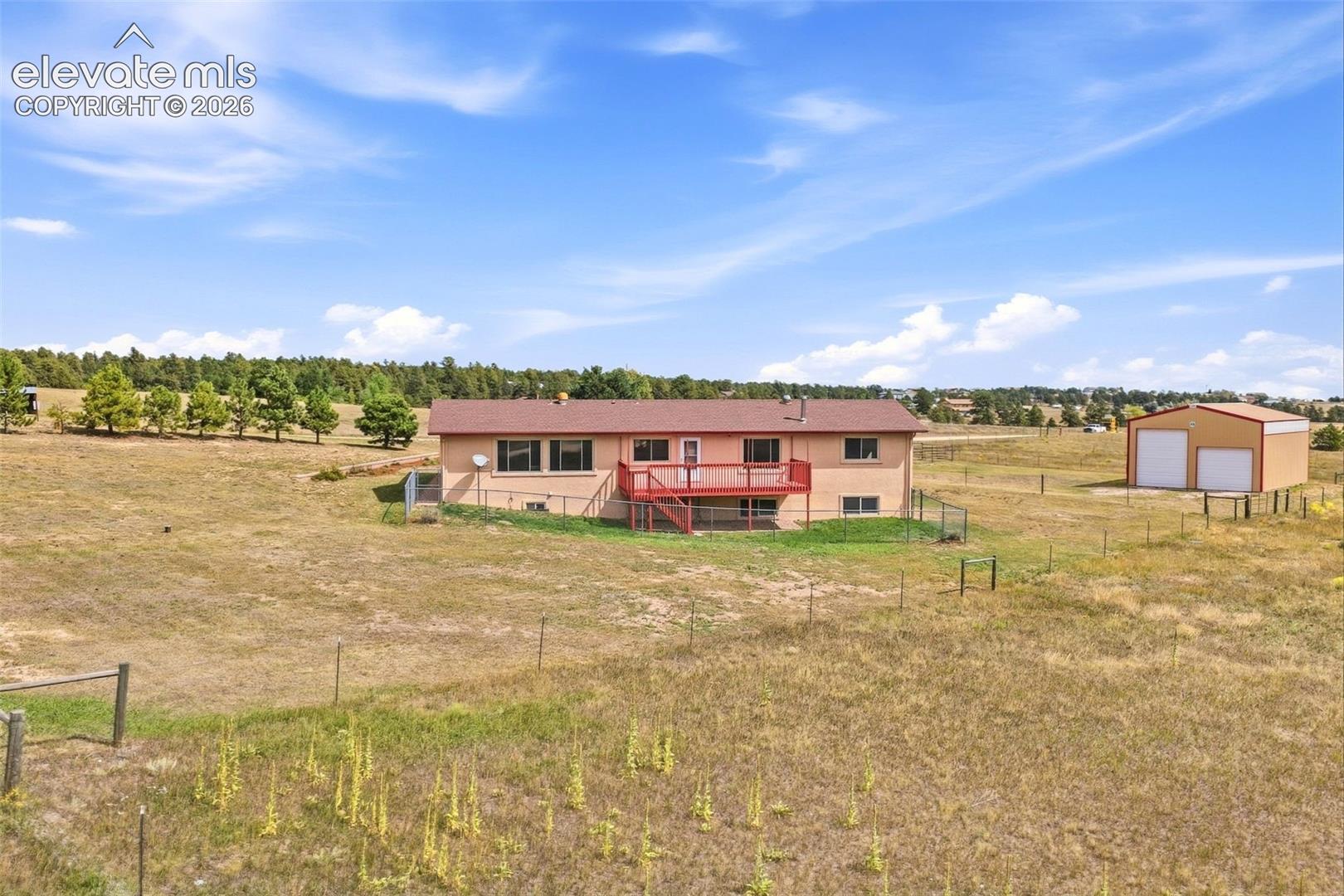 Expansive property featuring a ranch-style residence with a red deck, a detached metal outbuilding with two garage doors, and natural landscaping