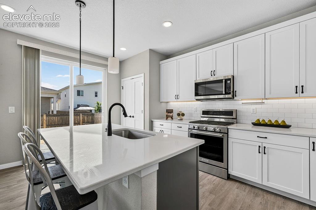 Modern kitchen featuring a large center island with integrated sink, pendant lighting, stainless steel appliances, white shaker cabinetry, and a subway tile backsplash