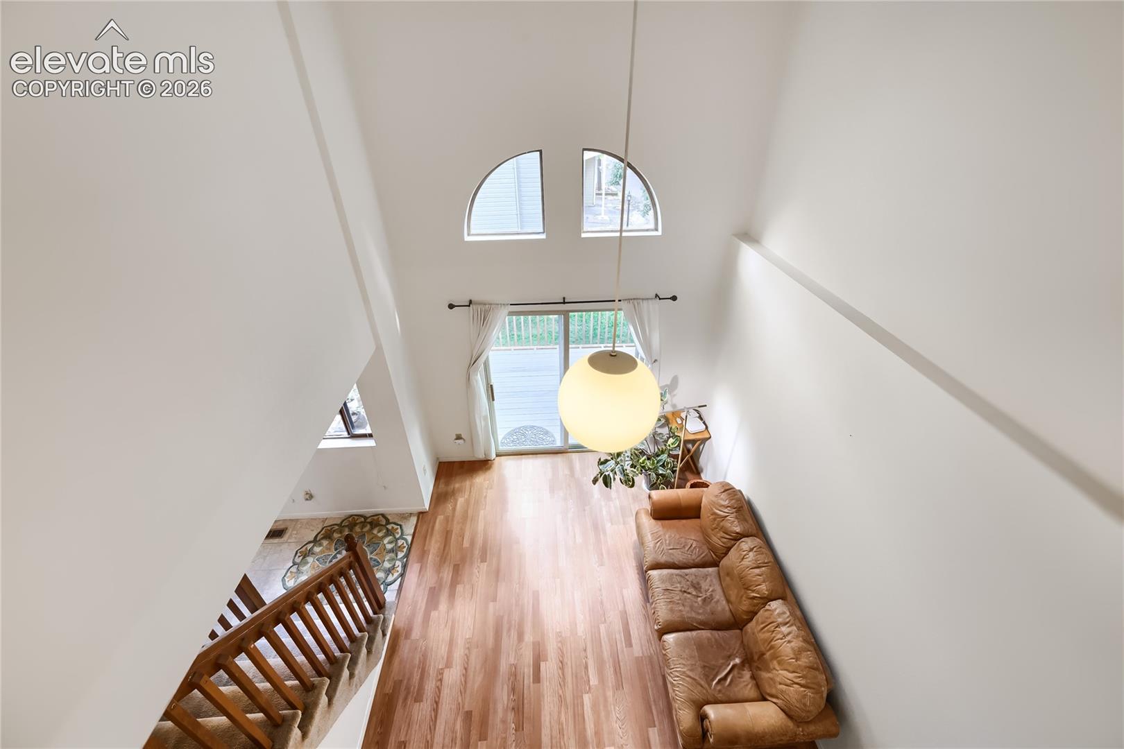 High ceilings with an exposed beam and arch-top window, wood-finish flooring, and a glass-paneled sliding door