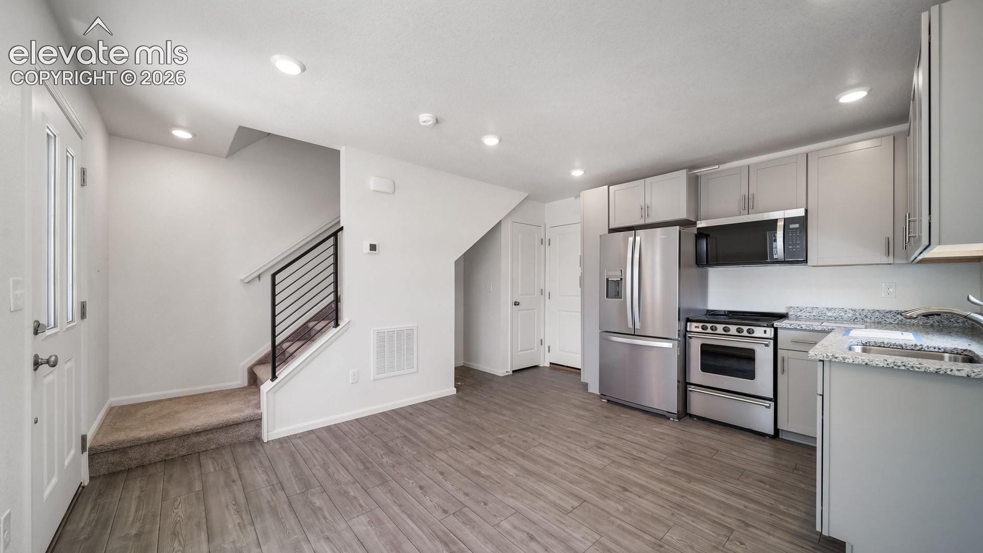 Stainless steel appliances, wood-finish flooring, recessed lighting, light gray cabinetry, and a contemporary staircase with metal railings
*photos of a model home*