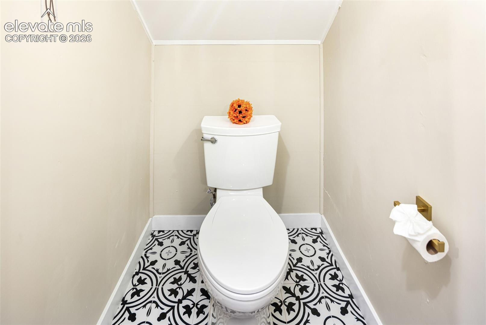 Bathroom featuring a toilet with a decorative patterned tile floor, light neutral walls, and white trim