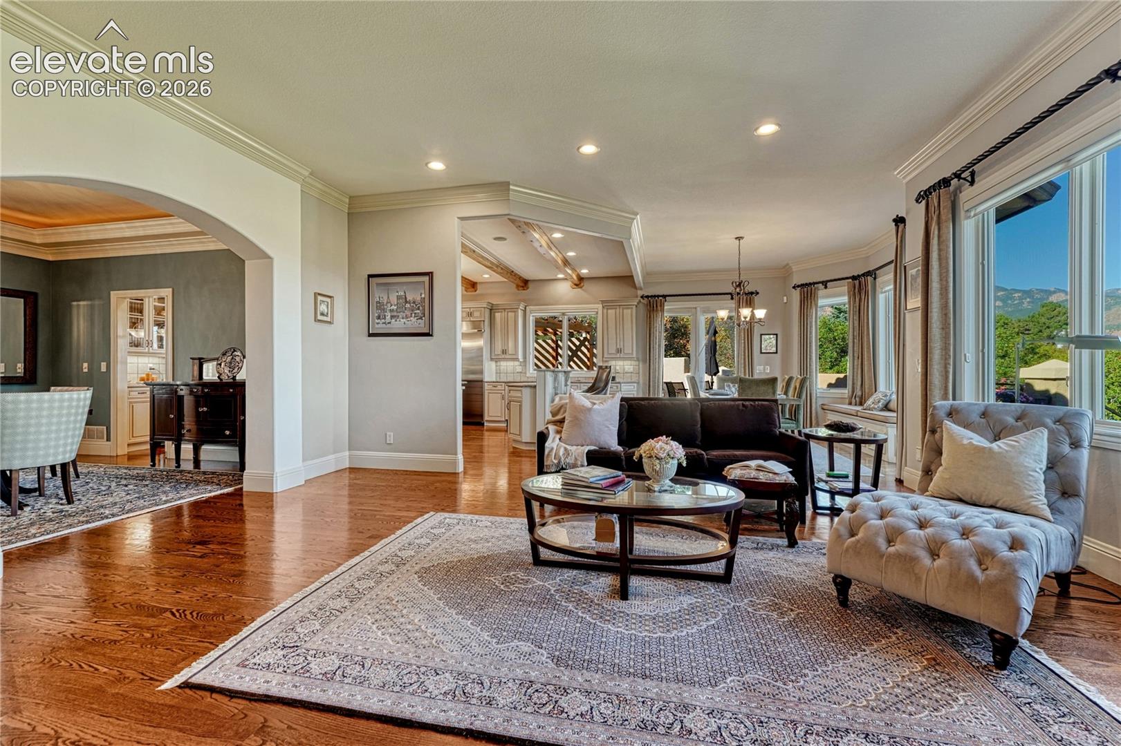 Open-concept living space featuring wood-finish flooring, crown molding, arched room entries, recessed lighting, and expansive windows