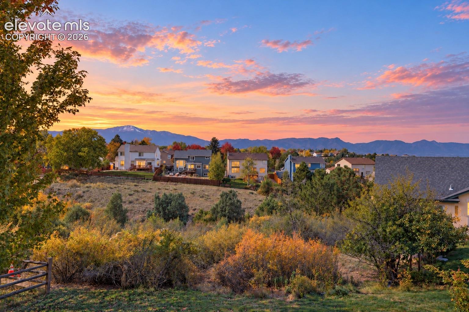 Residential area featuring mature trees, diverse native shrubbery, and mountain range backdrop under a sunset sky
