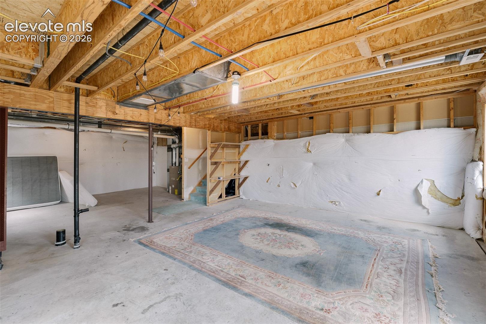 Unfinished basement with exposed wood joists, concrete flooring, and visible utility lines