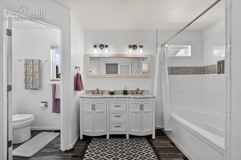 Dual vanity with stone countertop, tile flooring, and a shower-tub combination with tiled surround