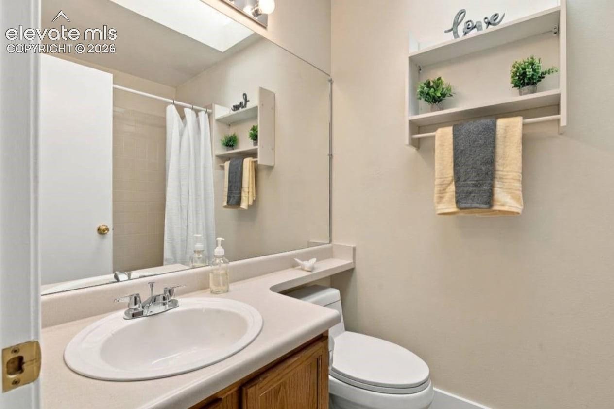 Bathroom featuring an expansive wall mirror, a wood-finish vanity cabinet with a solid-surface countertop, an integrated oval sink, and a built-in wall-mounted shelving unit