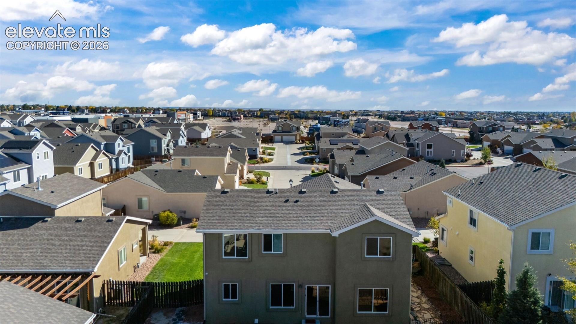 Aerial perspective of a multi-story residence featuring a shingled roof, stucco siding, and a fenced yard with hardscaping