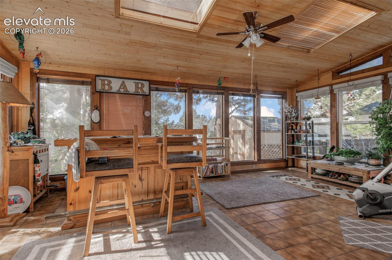 Wood-paneled ceiling with a built-in ceiling fan, skylights, and multiple large windows