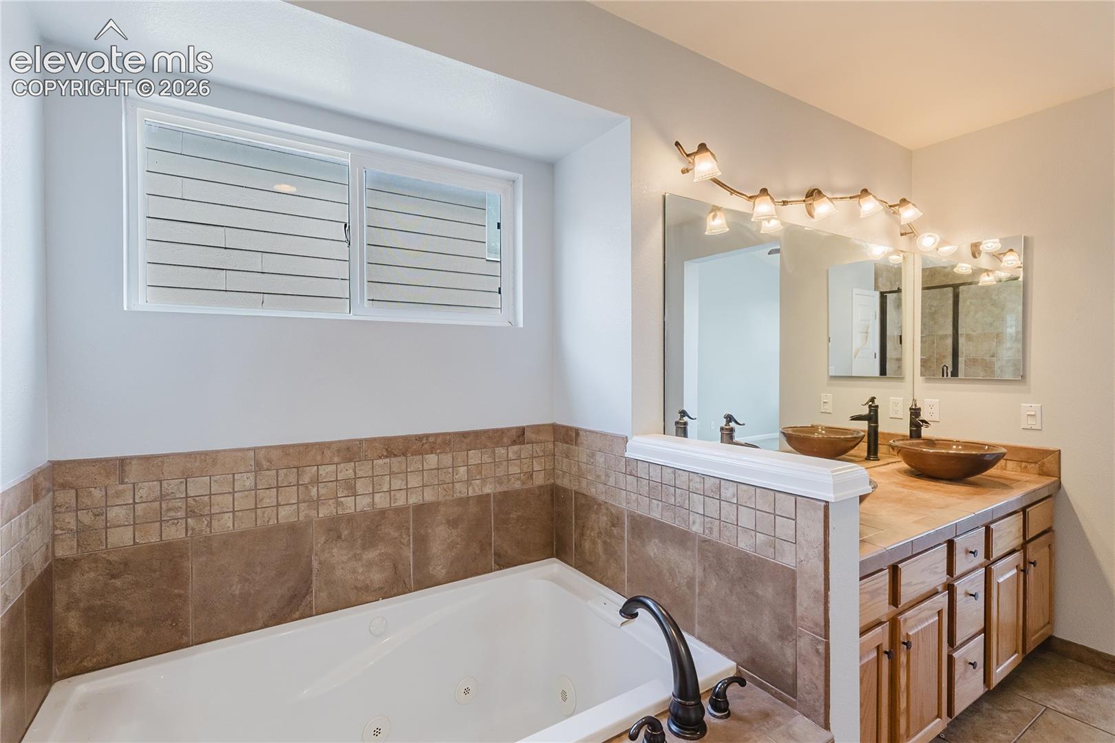 Spa-inspired primary bathroom featuring dual vanities with wood cabinetry, ceramic tile wainscoting, and a soaking tub