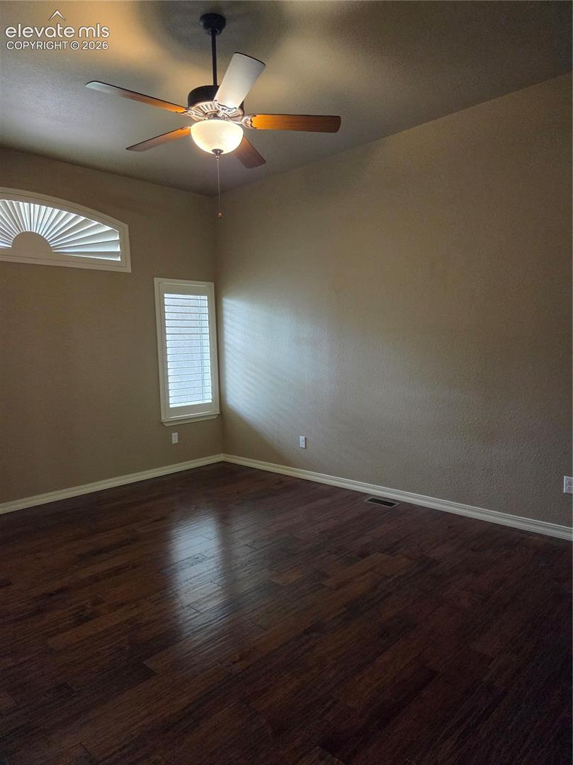 OPEN- Wood-finish flooring throughout, featuring a ceiling fan with integrated lighting, a rectangular window with louvered shutters, and an arched transom window