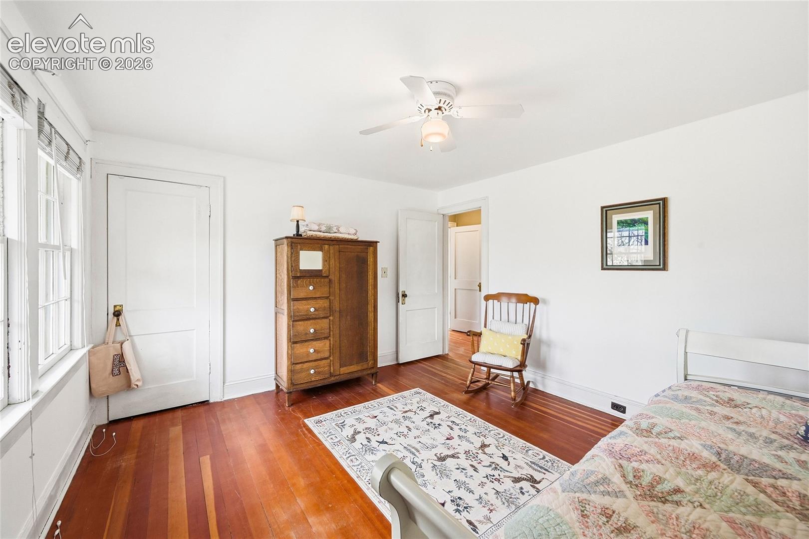 Interior space featuring wood-finish flooring, multi-pane windows, five-panel doors with brass hardware, and a ceiling fan with integrated lighting