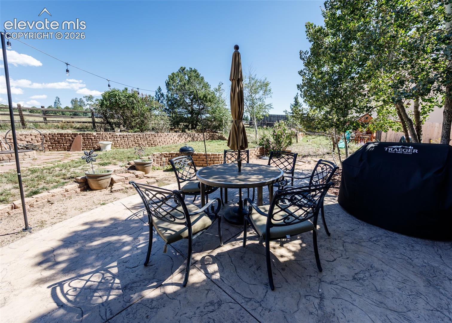 Stamped concrete patio with a tiered retaining wall, string lighting, and mature trees