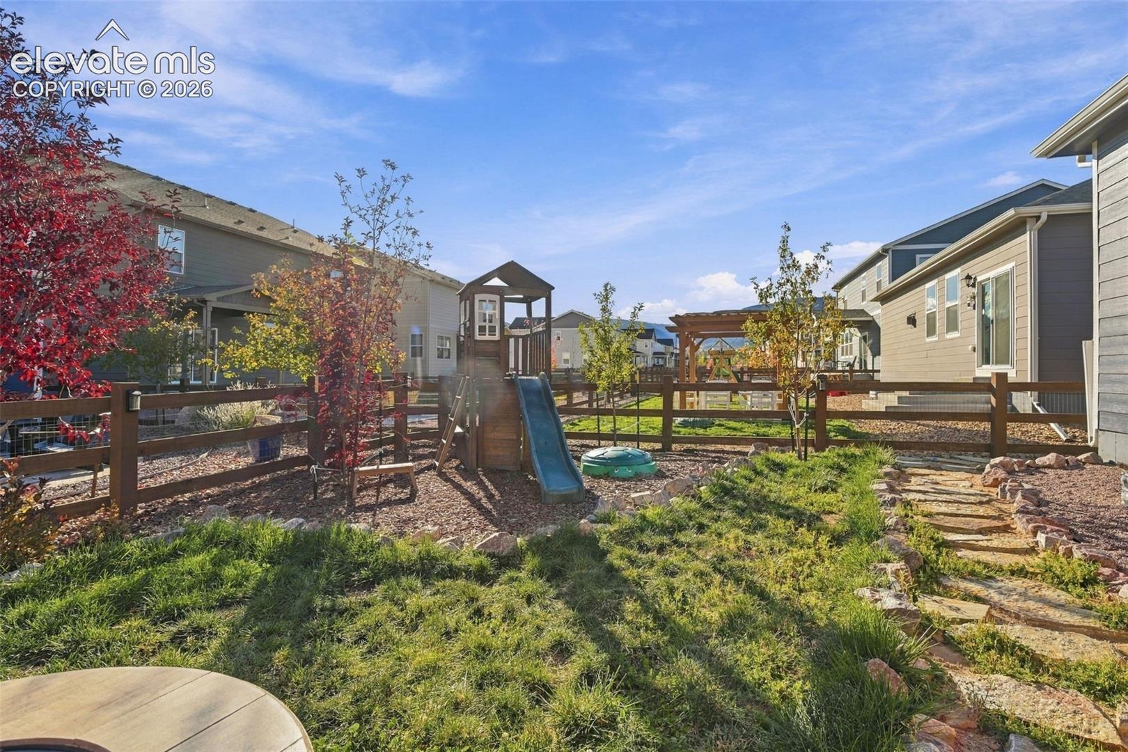 Backyard featuring a wood rail fence, stone paver pathway, mature trees, and a wooden pergola