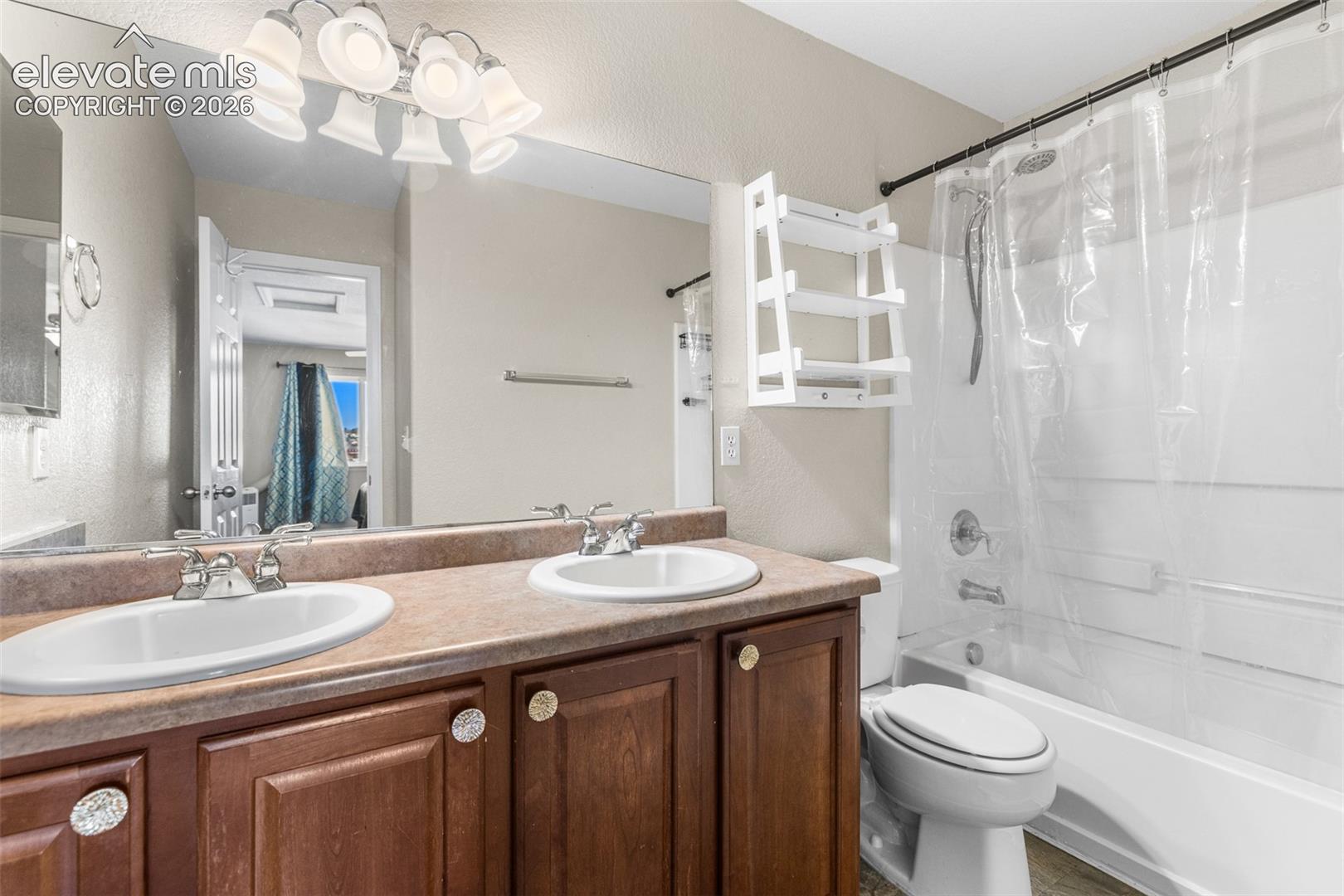 Dual-sink vanity with a solid-surface countertop, wood cabinetry, large vanity mirror, multi-light fixture, and a full-size tub and shower combination