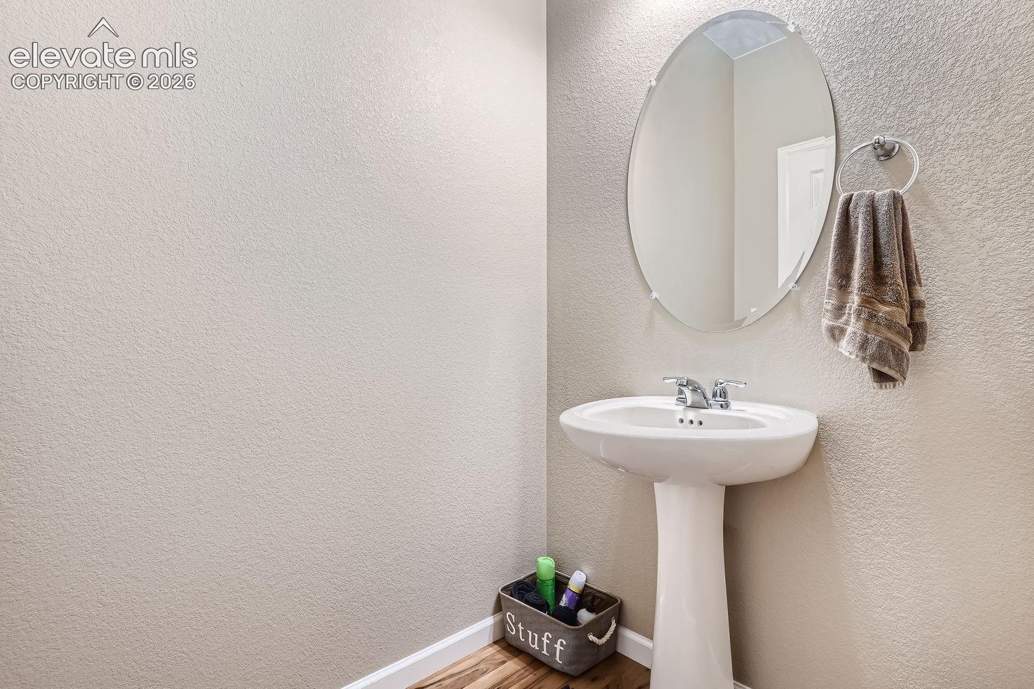White porcelain pedestal sink, oval frameless wall-mounted mirror, and chrome-finish faucet hardware