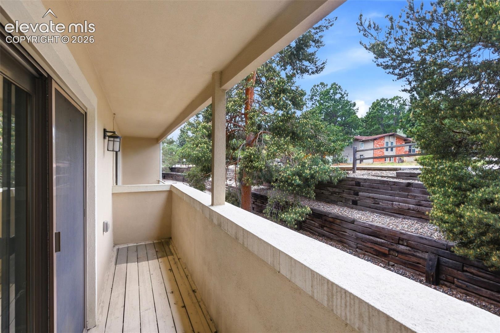 Covered exterior balcony with sliding glass door access, plank flooring, and an exterior wall lantern