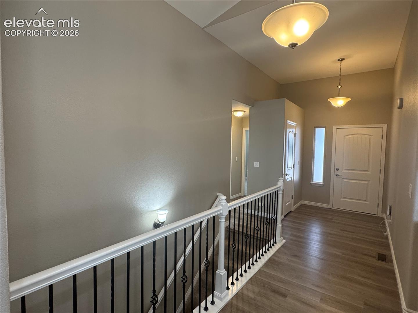 High-ceilinged entry featuring wood-finish flooring, white paneled door with a sidelight, iron and white spindle railing, and suspended semi-flush mount lighting