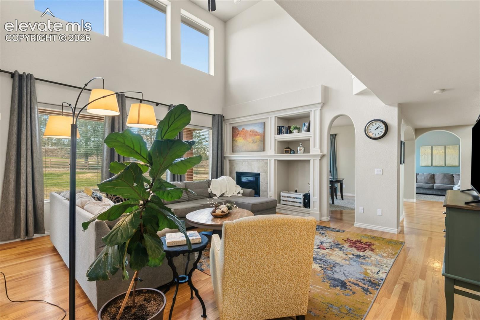 Vaulted living room with expansive windows, a built-in fireplace feature, archways, and wood-finish flooring