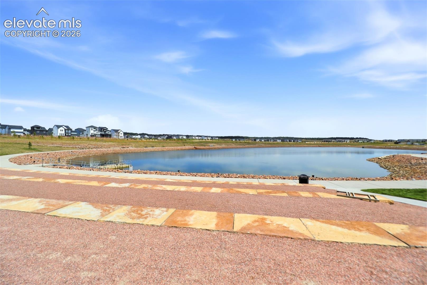 Paved pathways surround a calm lake, bordered by a landscaped rock embankment