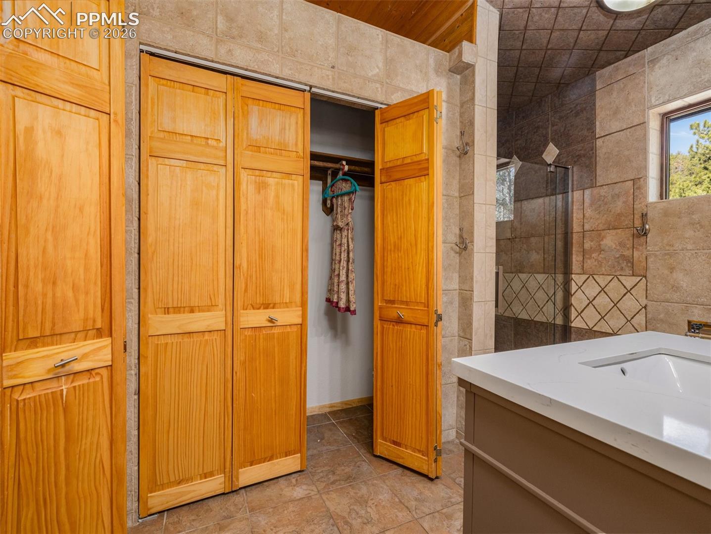 Bathroom with a closet, tile walls, vanity, and a tile shower