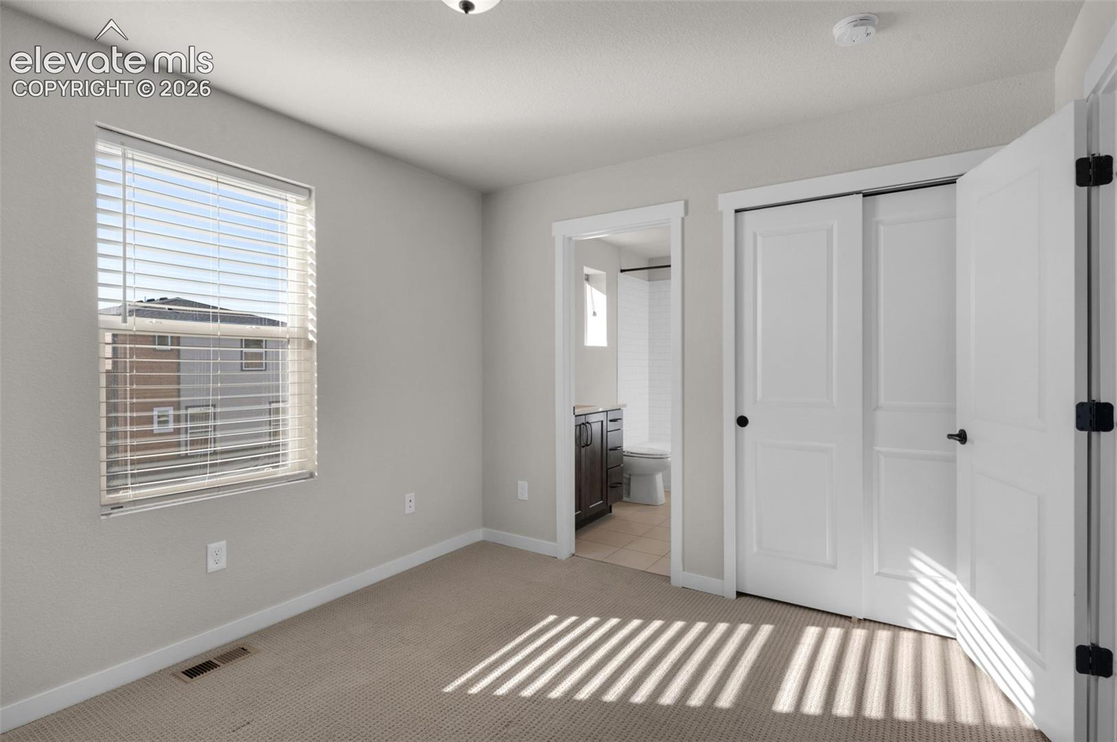 Carpeted flooring, window with blinds, bi-fold closet doors, additional doorway with dark wood-finish vanity