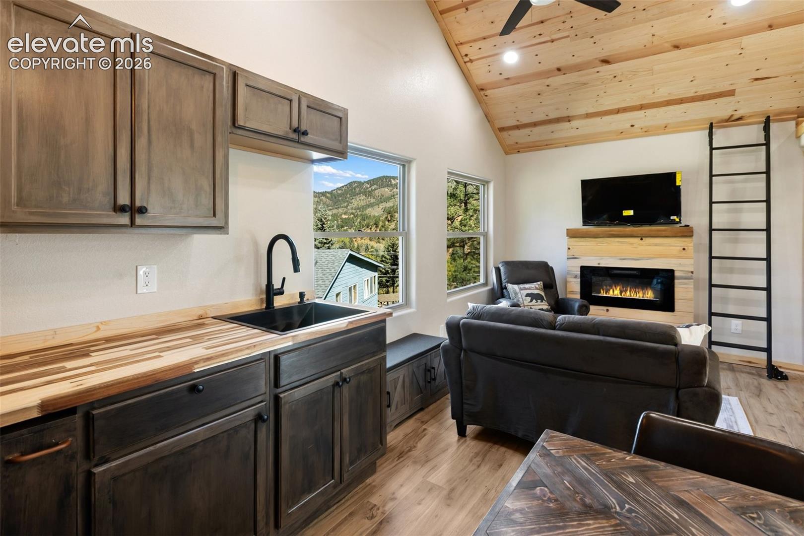 Vaulted ceiling with exposed wood planking, wood-finish flooring, built-in electric fireplace with wood surround, matte black hardware, and wood-surface countertops