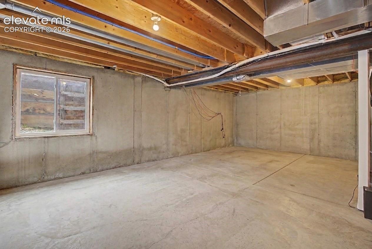 Concrete floor basement with exposed wood joist ceiling and a single window
