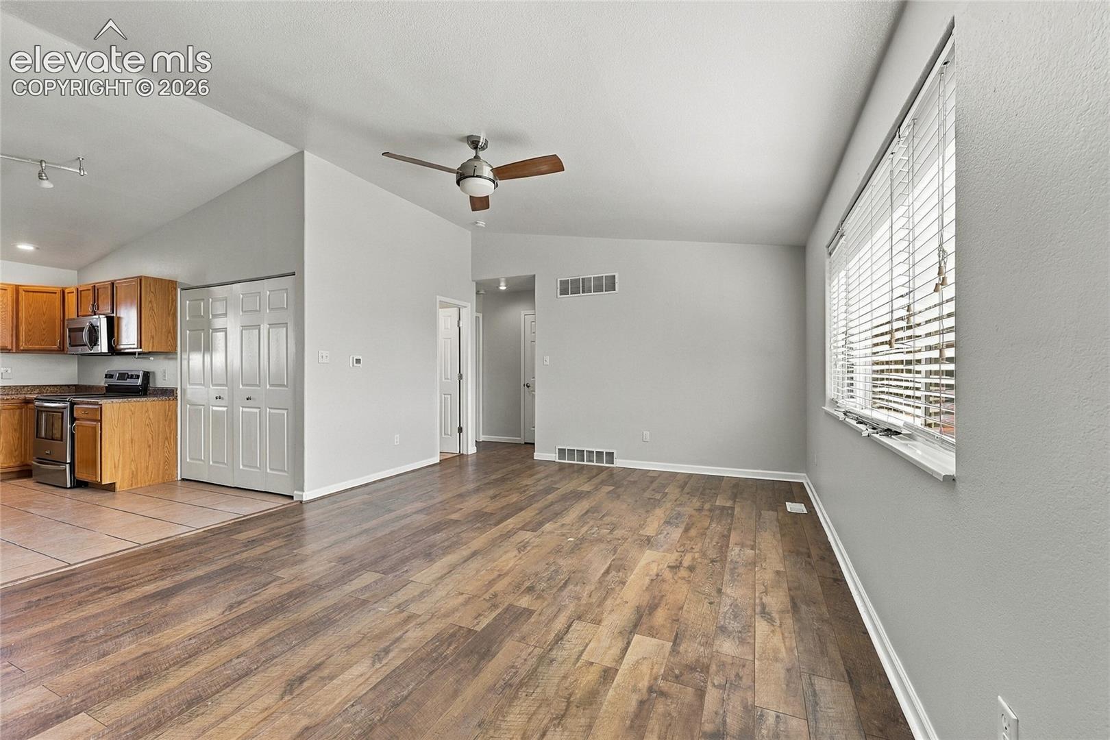 Open-concept interior featuring wood-finish flooring, vaulted ceilings, a ceiling fan, horizontal blinds, and natural wood cabinetry