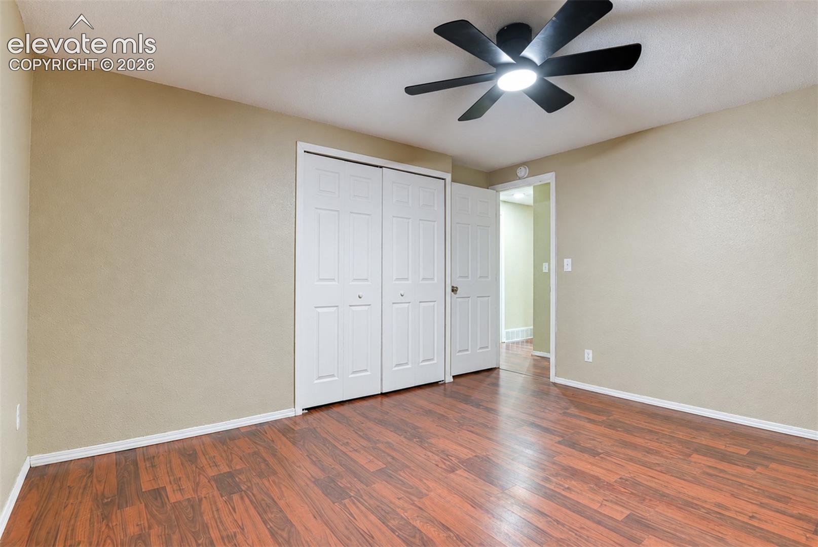 Room featuring wood-finish flooring, neutral wall paint, white baseboards, and a black ceiling fan with integrated lighting