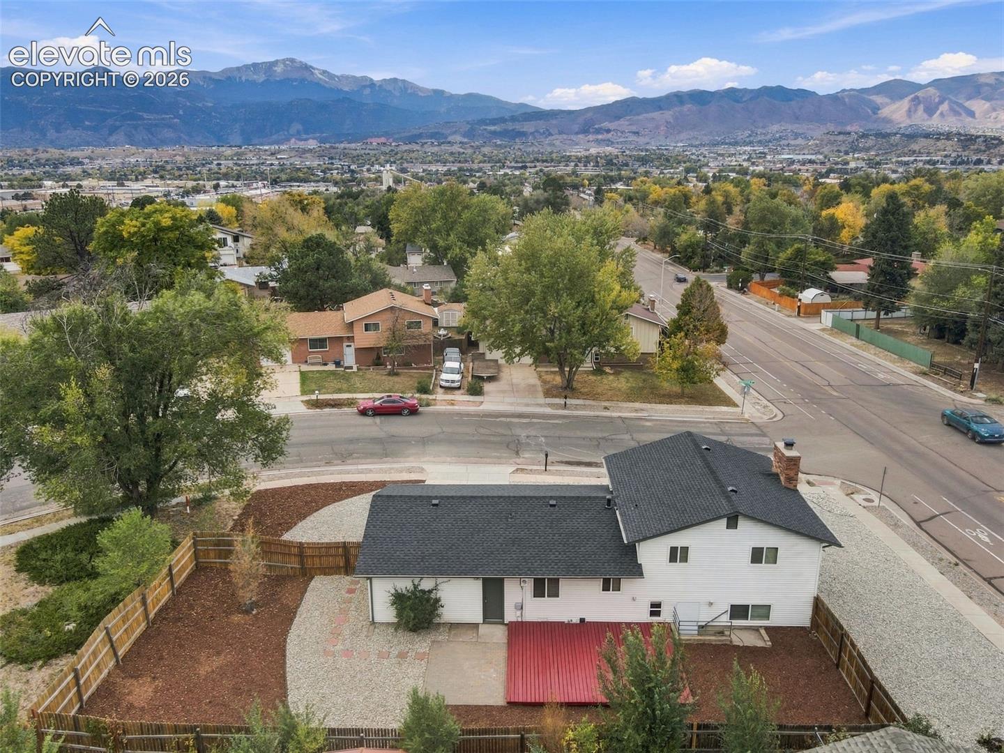 Aerial perspective of property featuring a multi-level residence with dark shingled roofing, a wood-fenced rear perimeter, and expansive mountain range scenery