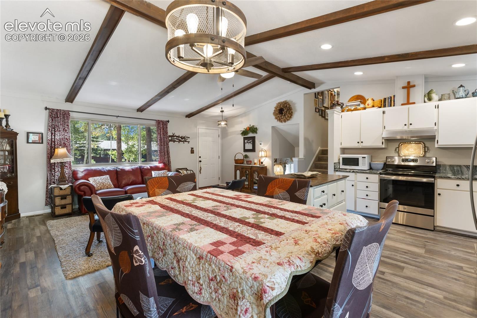 Vaulted ceiling with exposed wood beams, wood-finish flooring, white cabinetry, stainless steel appliances, and a built-in kitchen island