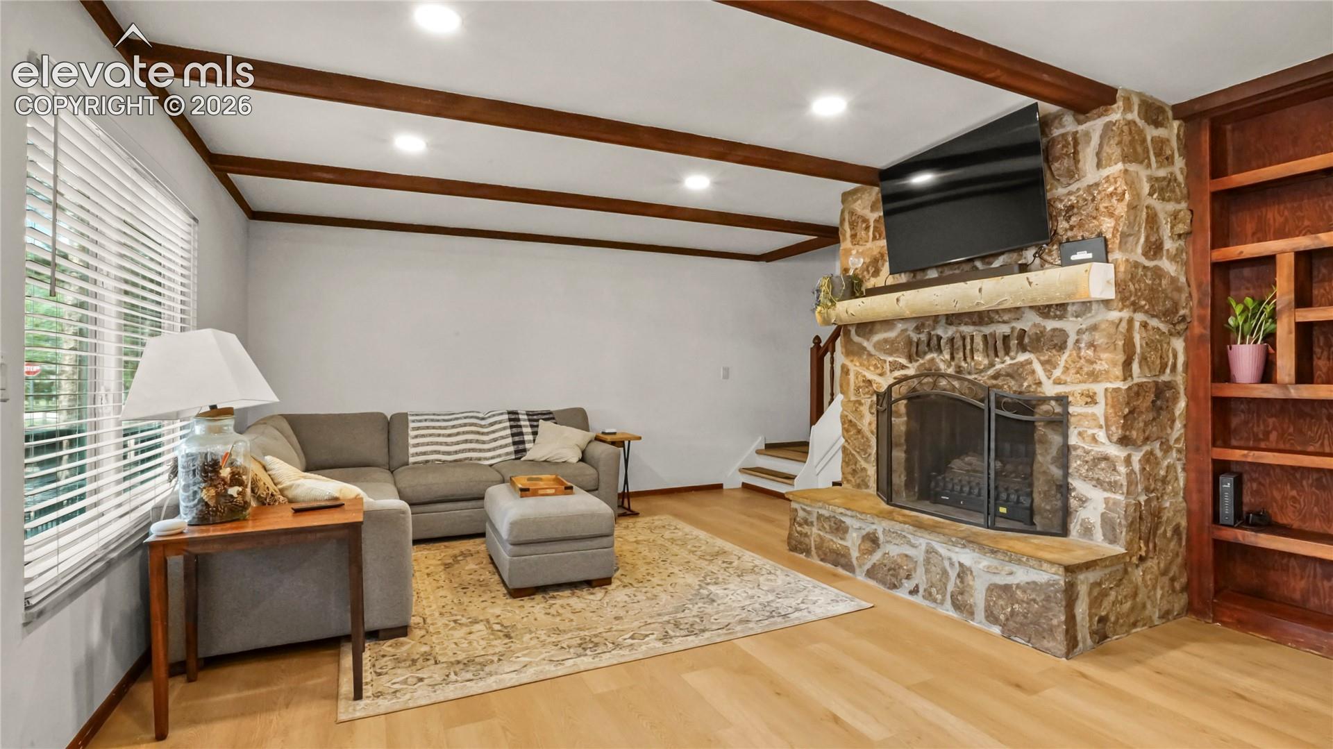LVP flooring, exposed ceiling beams, recessed lighting, stone-clad fireplace with mantel, and built-in shelving